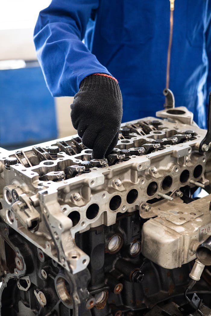 Close-up of a mechanic in gloves working on a car engine cylinder head in a workshop setting.